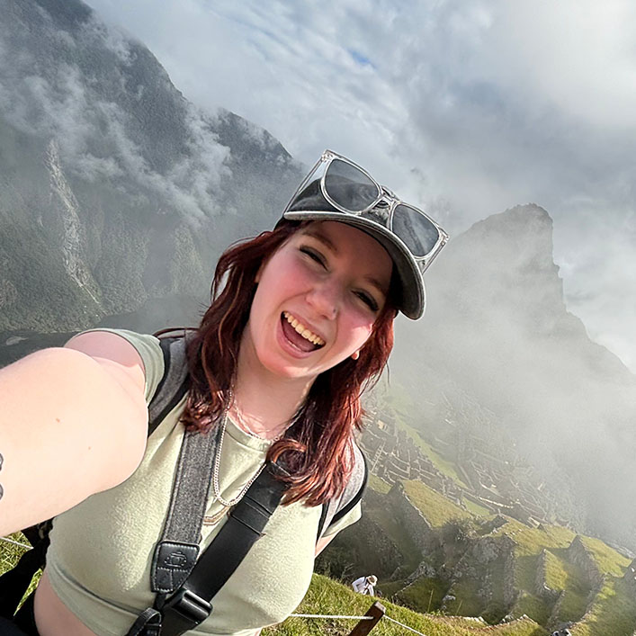 Girl with red-toned hair taking a selfie in front of Machu Picchu