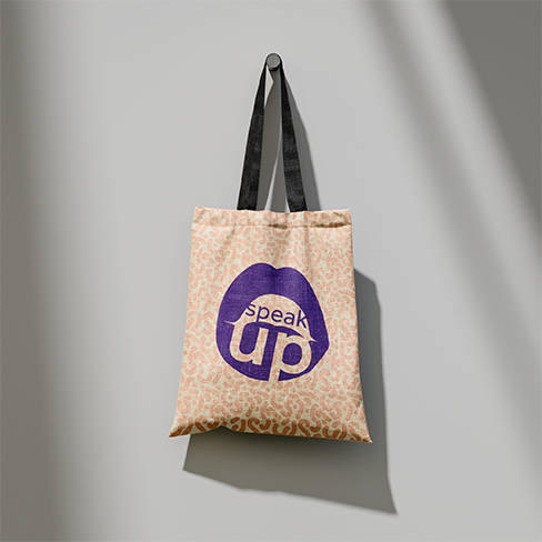 Tote bag with natural material hanging. Orange squiggle pattern is on the bag and the logo saying speak up is large and centred in purple