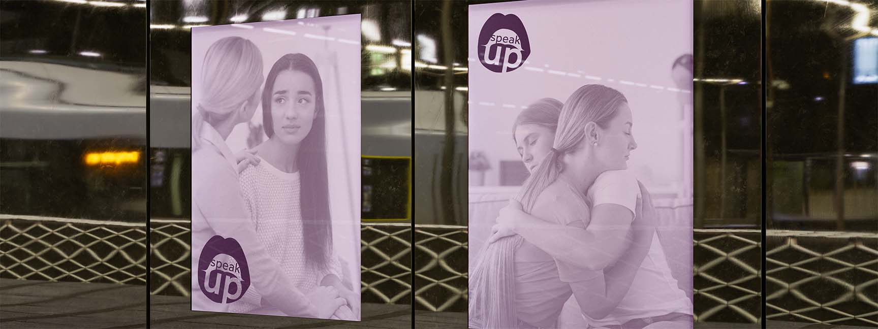 City environement where there is two large purple posters with the phrase: speak up start healing. They both have a photo of two women in an emotional conversation.
